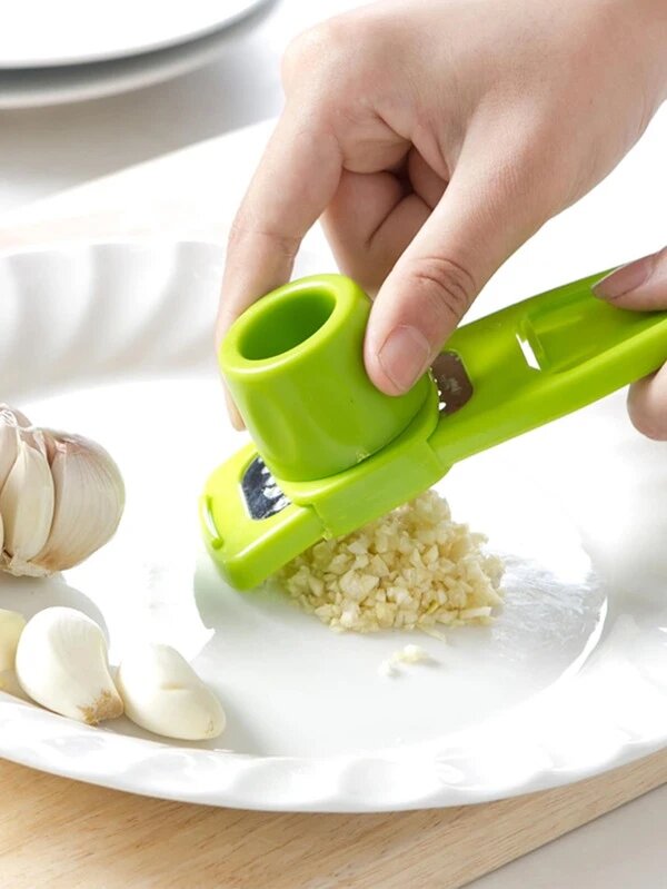 Green garlic press being used to crush garlic on a white plate.
